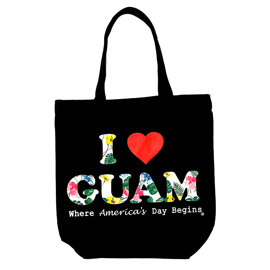 Black canvas tote bag featuring the ‘I ❤️ GUAM’ design with floral-patterned letters and the slogan ‘Where America’s Day Begins’ printed in white beneath the logo.