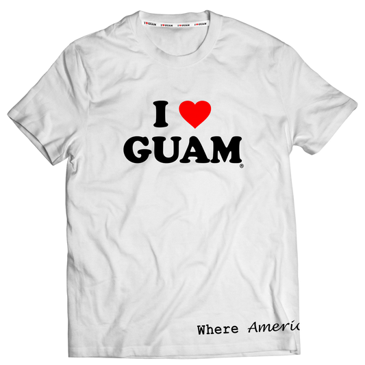 White unisex t-shirt with ‘I ❤️ GUAM’ design in bold black letters and a red heart, complemented by the phrase ‘Where America’s Day Begins’ at the bottom. The design emphasizes pride in Guam and its unique cultural identity.